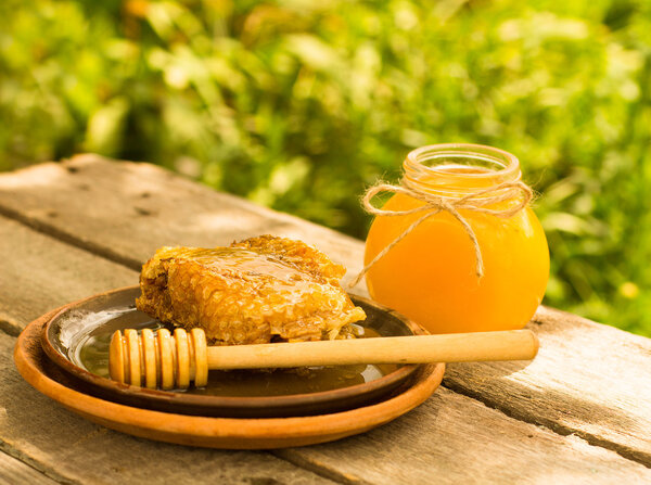 Honey in jar with honeycomb and wooden background.