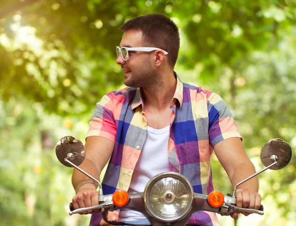 Красивый молодой человек в солнечных очках сидит на скутере — стоковое фото