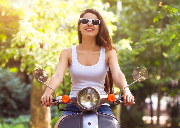 Happy young woman on a scooter on the street and smiling — Stockfoto