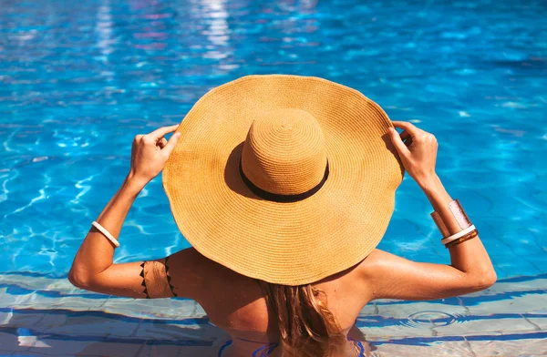 Beautiful woman wearing a hat and sunglasses, enjoying the pool