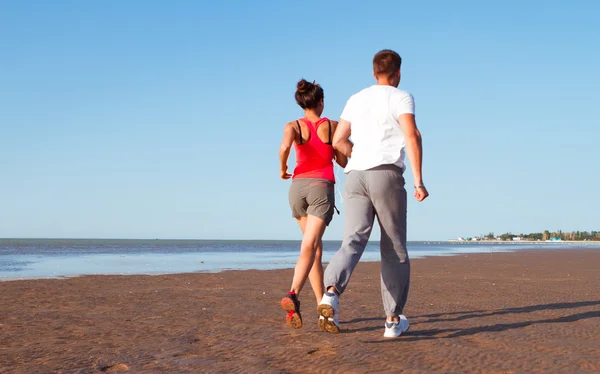 Νεαρό ζευγάρι τρέχει μαζί εκτός από το νερό στην παραλία. Άνθρωπος — Φωτογραφία Αρχείου