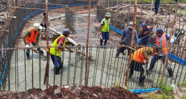 Endonezyalı veya Güneydoğu Asyalı inşaat işçileri beton dökerek, biçimlendirmenin içindeki taze çimento karışımını çelik takviyesi (inşaat demiri) ile dengeliyor.