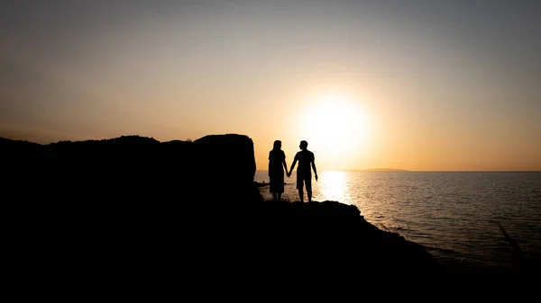 海のそばで日没時に手をつないでいる恋人たち — ストック写真
