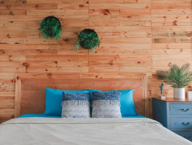 Ahşap yatak odasının iç kısmında mavi yatak ve yastıklar, beyaz battaniyeler ve yatak odasını süslemek için saksı bitkileri bulunuyor..