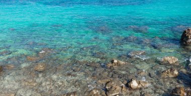 Turkuaz bir denizin görüntüsü öyle berrak ki kayaların arka plan görüntüsü olarak kullanılabileceğini görebilirsiniz..