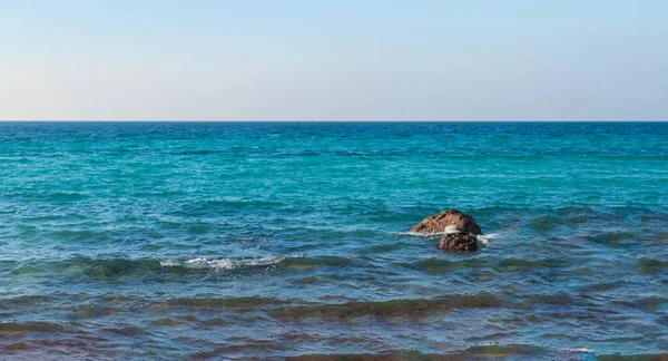 Parlak gökyüzüne karşı kayaları olan turkuaz bir denizin manzarası arka plan görüntüsü olarak kullanılabilir..