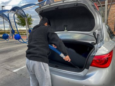Elektrikli hortumla arabasını elektrikli süpürgeyle süpürüp park yerine götüren bir adamın yakın görüntüsü.