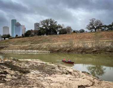 Buffalo Bayou Parkı manzarası. Teksas 'ın arka planında, binaların ve ağaçların önünde insanlar kayıkla geziyor.
