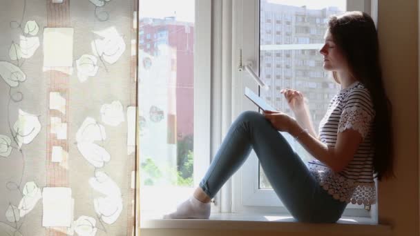 Mooie jongedame met tablet op de vensterbank — Stockvideo