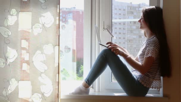 Teen flicka sitter på ett fönster fönsterbräda och arbeten på hennes notebooke — Stockvideo