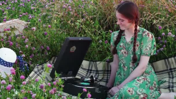 Молодая девушка на пикнике на лугу слушает пластинку на винтажном граммофоне — стоковое видео