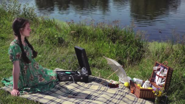 Chica joven en el picnic en el río escuchando el disco en el gramófono vintage — Vídeo de stock