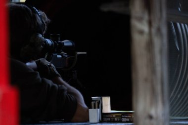 Kanada, 10 Eylül 2025: Odaklanmış nişancı dürbünden dürbüne nişan alıyor loş ışıklı kabin içinde