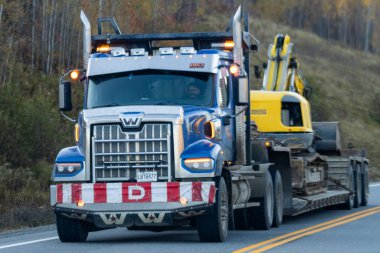 Kanada, 11 Ekim 2025: Sarı kazıcıyı dolambaçlı yolda taşıyan büyük mavi nakliye kamyonu