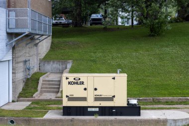 Kanada, 24 Temmuz 2025: Binanın yanında büyük endüstriyel jeneratör, çimenli tepeye park edilmiş arabalar.