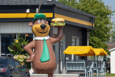 Kanada, 09 Ağustos 2025: Çizgi film ayı heykeli restoranın önünde sarı tenteli hamburger tutuyor
