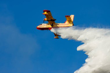 Kanada, 17 Ekim 2025: Sarı itfaiye uçağı açık mavi gökyüzü arka planına su bırakıyor