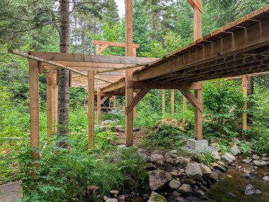 Kanada, 28 Temmuz 2025: Nehrin yanındaki yemyeşil ormanın ortasında ahşap köprü inşaatı