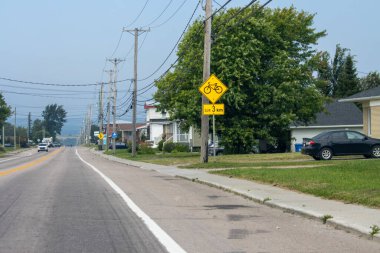 Kanada, 09 Ağustos 2025: Banliyö caddesi boyunca kaldırımlı ve ağaçlı bisiklet uyarısı
