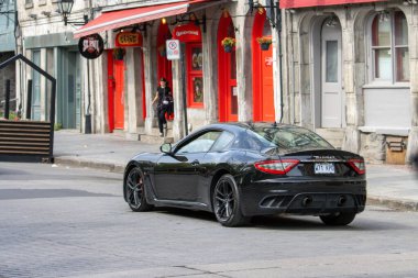 Quebec, Kanada, 05 Temmuz 2025: Büyüleyici mahalle caddesinde kırmızı vitrinin yakınına park edilmiş siyah spor araba