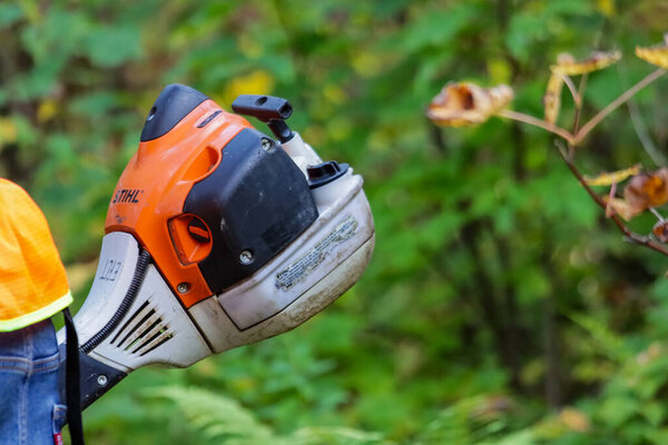Канада, 26 сентября 2025 года: Рабочий с оранжевым и черным электроинструментом в пышной лесной зоне