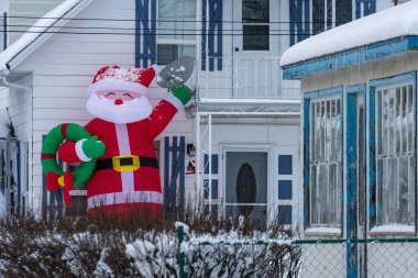 Kanada, 12 Kasım 2025: Dev şişme Noel Baba, karlı mahalleyi mavi kepenkli evden selamlıyor