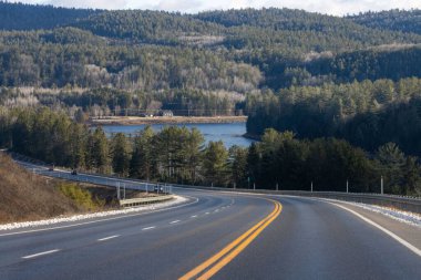 Kanada, 08 Kasım 2025: Virajlı yol ormanlık tepelere, göle ve uzak binalara gidiyor