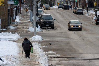 Kanada, 13 Kasım 2025: Yaşlı kadın kış sabahı gökyüzü altında karlı şehir kaldırımında yürüyor