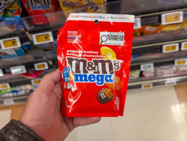 Kanada, 02 Kasım 2025: Bir el mağaza koridorunda kırmızı fıstık ezmesi mega şeker poşetini tutuyor