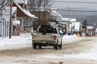 Kanada, 10 Kasım 2025: Kamyon karlı yerleşim sokağında tüm arazi araçlarını taşıyarak ilerliyor.