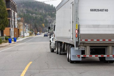 Kanada, Quebec, 29 Ekim 2025: Ağaçlarla dolu sessiz bir yerleşim yerinden geçen büyük beyaz kamyon