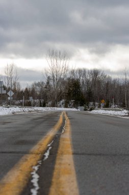 Kanada, Quebec, 29 Kasım 2025: Kış yolu bulutlu gökyüzü altında kıvrımlı, sarı çizgiler ileriye doğru ilerliyor
