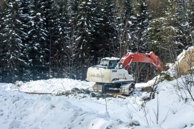 Kanada, Quebec, 05 Aralık 2025: Kışlık inşaat projesi sırasında karlı ormanda çalışan kazıcı