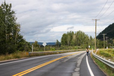 Kanada, Quebec, 07 Eylül 2025: Virajlı bir kırsal yol boyunca seyahat eden tek bir bisikletçi.