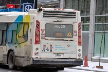 Kanada, Montreal, 22 Aralık 2025: Renkli tasarım, reklamlar, kar ve tabela ile şehir kış otobüsü