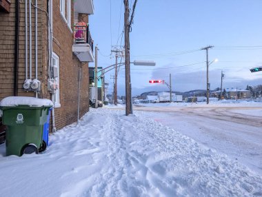Kanada, Quebec, 01 Aralık 2025: Tuğla binanın yanında karlı kaldırım, kavşakta parlayan trafik ışıkları
