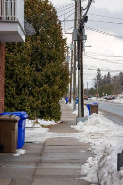 Kanada, Quebec, 27 Kasım 2025: Geri dönüşüm kutuları, elektrik hatları ve ağaçlarla kaplı karlı kaldırım