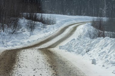 Kanada, Quebec, 05 Aralık 2025: Yalnız toprak yol kış günü karlı ormanda dönüyor