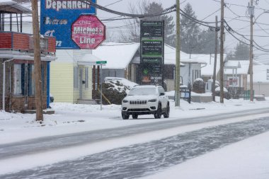 Kanada, Quebec, 30 Kasım 2025: Sessiz küçük kasaba sokağına kar yağarken park edilmiş beyaz cip