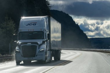 Kanada, Quebec, 08 Kasım 2025: Bulutlu gökyüzünün altında ıslak dağ yolu boyunca giden yük kamyonu