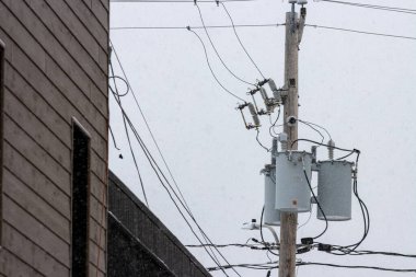 Kanada, Quebec, 30 Kasım 2025: Duvarın yanında transformatörlerle birlikte elektrik direğine kar yağıyor