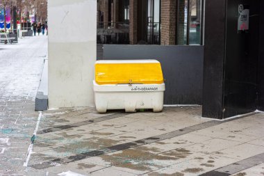 Kanada, Montreal, 22 Aralık 2025: Karlı kentsel kaldırım köşesinde sarı kaygan tuz konteynırı