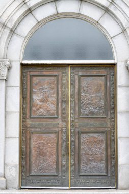 Kanada, Quebec, 27 Kasım 2025: Entrika oymalı bronz çift kapı Kemerli buzlu pencerenin altında.