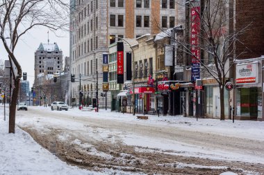 Kanada, Montreal, 25 Aralık 2025: Dükkanları, arabaları ve yüksek binaları olan karlı şehir caddesi
