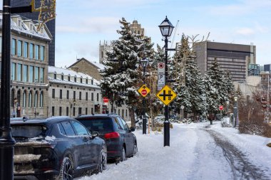 MONTREAL, CANADA, 24 Aralık 2025: Kış şehri sokağı, karla kaplı yol, park edilmiş arabalar, tarihi binalar, kentsel kış manzarası, sokak tabelaları, sokak lambaları, mavi gökyüzü, kardaki ağaçlar