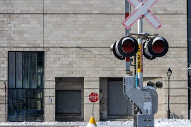 MONTREAL, CANADA, 24 Aralık 2025: Demiryolu geçiş işareti, şehir kış manzarası, tuğla bina, dur işareti, kar, acil iletişim bilgileri