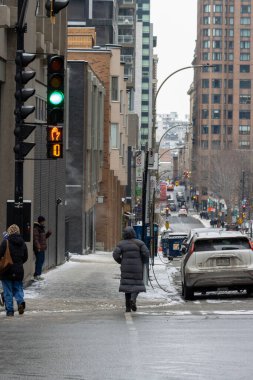 Kanada, Montreal, 23 Aralık 2025: Kentsel kış sahnesi yayaları karlı şehir caddesi kavşağını geçiyor