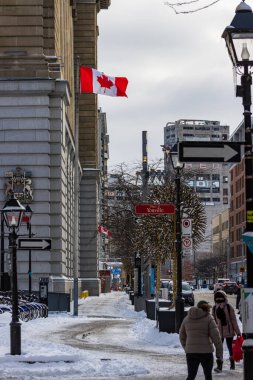 Kanada, Montreal, 24 Aralık 2025: Kanada kış kentsel caddesi, yayalar yürüyor, bayraklar dalgalanıyor, karlar kaplanıyor.