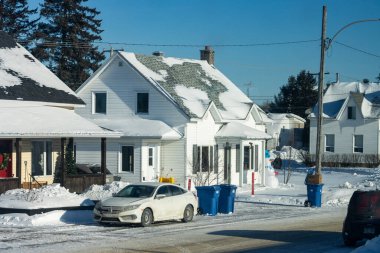 MONTREAL, CANADA, 26 Aralık 2025: Karlı banliyö, beyaz ev, park edilmiş arabalar, mavi çöp kutuları, kardan adam