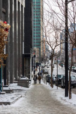 Kanada, Montreal, 23 Aralık 2025: Yürüyen ve yüksek binaları olan karlı şehir caddesi